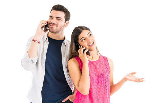 Beautiful woman and handsome man using their mobile phones for communicating while standing against white background