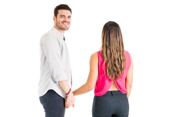 Happy Latin man holding girlfriend's hands while standing against plain background