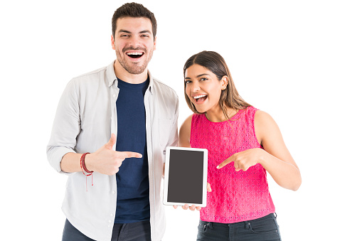 Cheerful young couple pointing at digital tablet with blank screen against white background