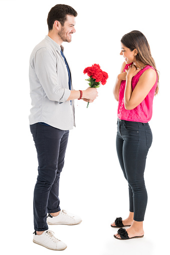Full length of Latin man giving flower bouquet to amazed girlfriend over white background