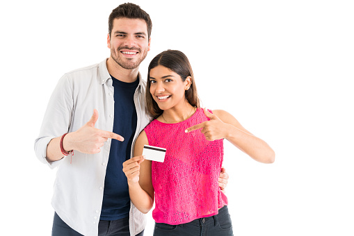 Latin couple smiling while pointing at credit card against white background