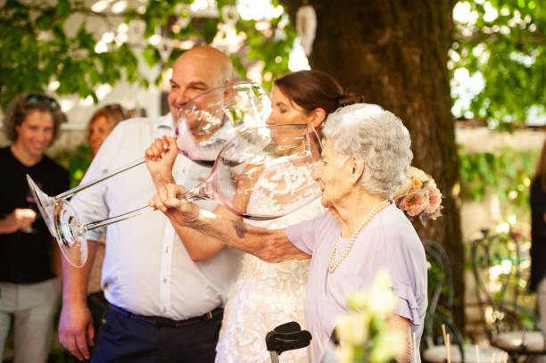 Bride and Her Mother in Law Drinking Wine From Large Wineglass at Wedding Celebration Bride and Her Mother in Law Drinking Wine From Large Wineglass at Wedding Celebration couple drinking stock pictures, royalty-free photos & images