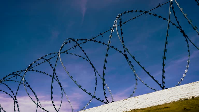 The fence with barbed wire on the background of a gloomy cloudy dark blue sky.