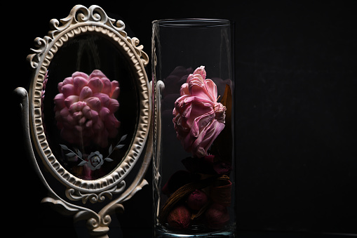 A pink flowers reflection in a Vintage Oval Desk Mirror with white frame on black background