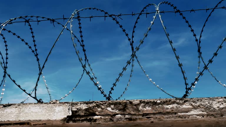 The fence with barbed wire on the background of a gloomy cloudy dark blue sky.