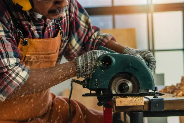 senior male carpenter using circular saw to make woorwork in workshop as hobby