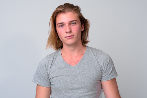 Studio shot of young handsome man with long blond hair against white background