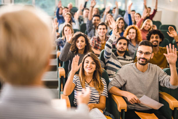 istock Happy college students raising their hands on a class at lecture hall. 1161095812