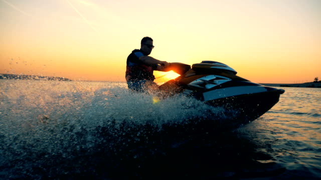 A man is riding a jet-ski along the coastline during sunset