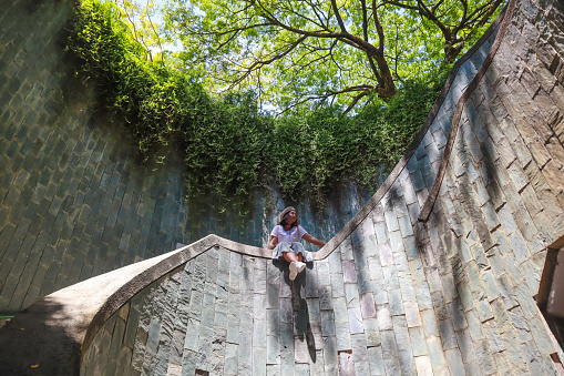 A young asian woman  tourist sat  standing on the staircase at Underground spiral staircase at Fort Canning Park, Landmark and popular destination in Singapore