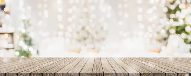 Photo of Empty woooden table top with abstract warm living room decor with christmas tree string light blur background with snow,Holiday backdrop,Mock up banner for display of advertise product.