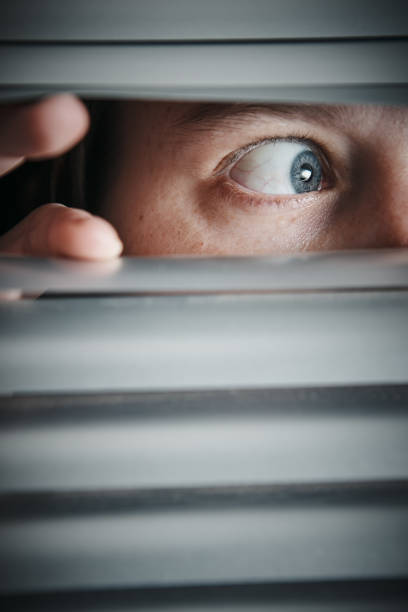 istock Frightened female looks sideways through Venetian blinds 1161115739