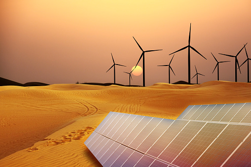 Renewable energy with windmills and solar panels in desert at sunset