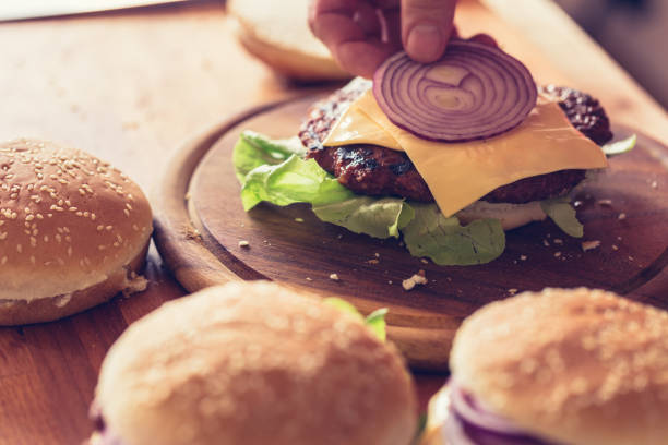 istock Hamburger preparing, slice of red onion put on burger bun, close-up 1161120217
