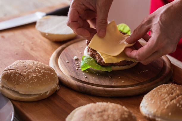 Hamburger preparing, sheet of soft cheese put on burger bun, close-up