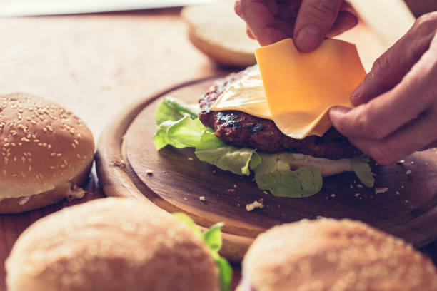 istock Hamburger preparing, sheet of soft cheese put on burger bun, close-up 1161120275