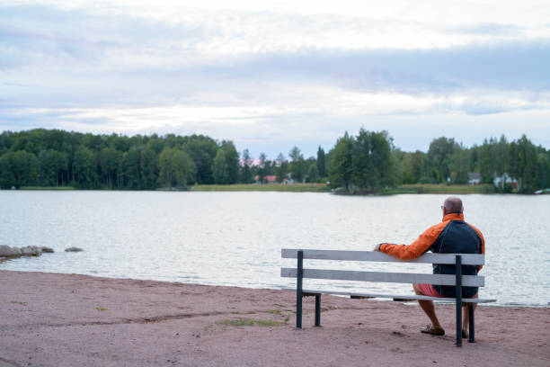 istock Senior Man Sitting On The Bench By The Lake 1161135525