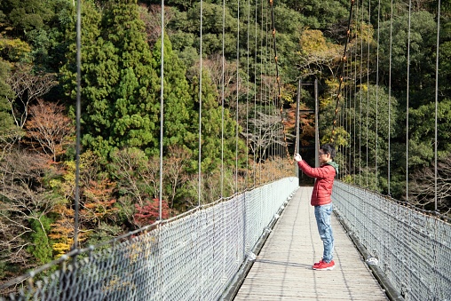 A traveler standing on a cable bridge near a mountain, taking a photo of the surrounding view.