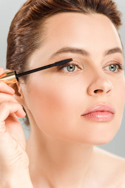 istock attractive woman applying mascara isolated on grey 1161143553