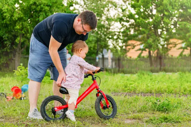 Photo of Young father spend time with Cute little one years old toddler girl child and balance bike, father's day