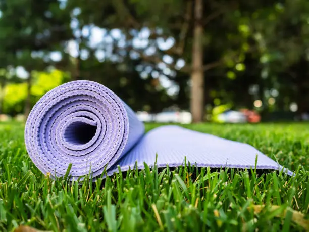 Mat for yoga or fitness. Purple rug on green grass in the shade of a tree. Healthy lifestyle