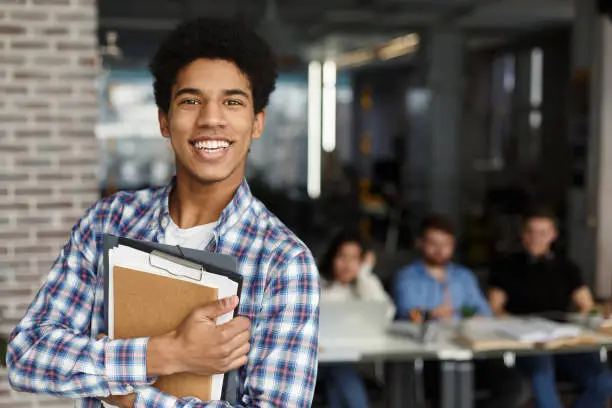 Photo of Happy student with books looking at camera in library