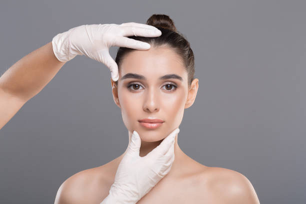medico in guanti toccare viso donna, sfondo grigio - plastic beauty injecting protective glove foto e immagini stock
