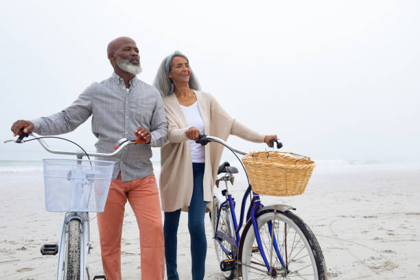 ビーチで自転車を持つカップル - retirement mature couple couple bicycle ストックフォトと画像