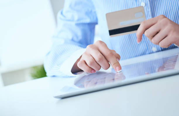 istock Woman's hands holding a credit card and using tablet pc for online shopping. Middle section of young businesswoman making online payments with credit card and tablet. 1161153422