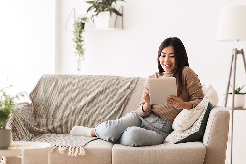 Asian Teenage Girl Watching Movie On Tablet, Resting at Home, Copy Space