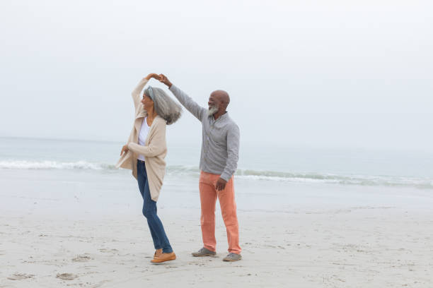 Couple dancing at the beach Front view of happy senior diverse Couple smiling at the beach. Authentic Senior Retired Life Concept middle aged couple dancing stock pictures, royalty-free photos & images
