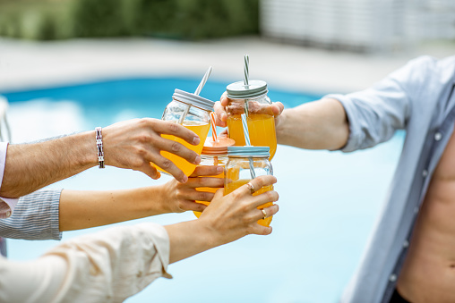 Friends clinking bottles with drinks on the swimming pool, close-up
