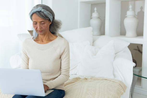 istock Woman sitting on a couch in a white room while using a white laptop 1161155866
