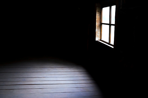 Darkness and horror, background with copy space. Inside in an empty dark room of an old abandoned house with black walls mystical light in the darkness of the window with a spot on the floor