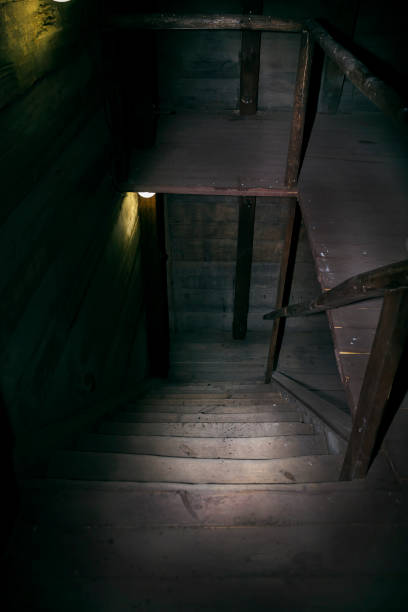 istock Darkness and horror in a ghostly building. Inside on a dark wooden staircase with steps down to the basement of an old abandoned house with black walls mystical light from a dim lamp on the floor 1161156337