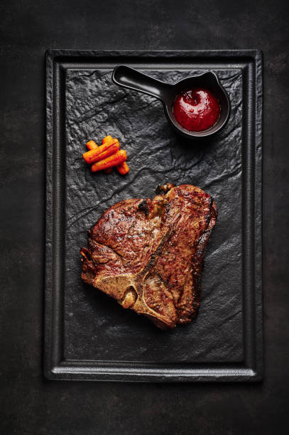 istock large beef t bone steak with sauce at black stone background. 1161157993