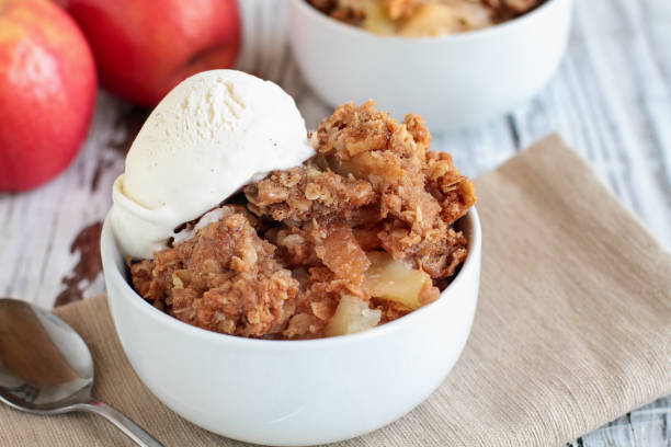 Fresh hot homemade apple crisp or crumble with crunchy streusel topping Fresh hot homemade apple crisp or crumble with crunchy streusel topping topped with vanilla bean ice cream over rustic white table. Selective focus with blurred background. cobbler dessert stock pictures, royalty-free photos & images