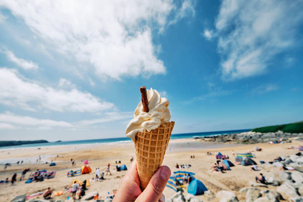 POV wide angle view of a hand holding Ice cream cone at Fistral Beach, Newquay on a sunny June day. stock photo