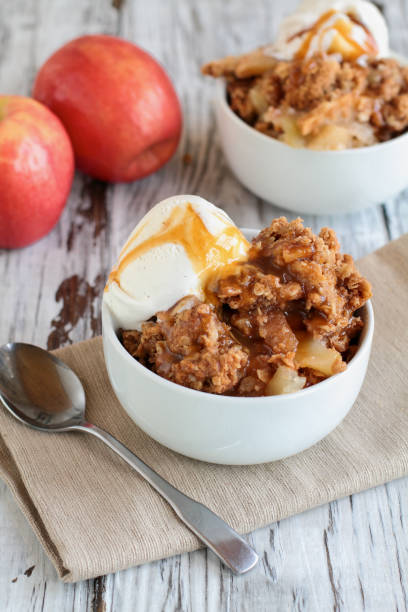 Fresh hot homemade apple crisp or crumble with crunchy streusel topping topped with vanilla bean ice cream and Caramel Sauce Fresh hot homemade apple crisp or crumble with crunchy streusel topping topped with vanilla bean ice cream and Caramel Sauce over rustic white table. Selective focus with blurred background. apple pie and ice cream stock pictures, royalty-free photos & images