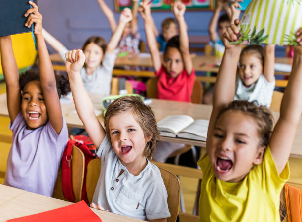 istock Group of joyful elementary students screaming with raised arms in the classroom. 1161167435