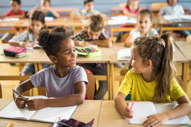 istock Happy schoolgirls talking to each other on a class at school. 1161168766