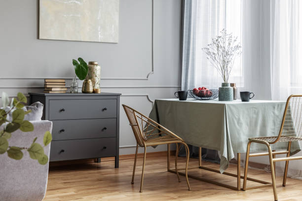 istock Dining room interior with long table, stylish golden chairs and grey wooden commode 1161169875