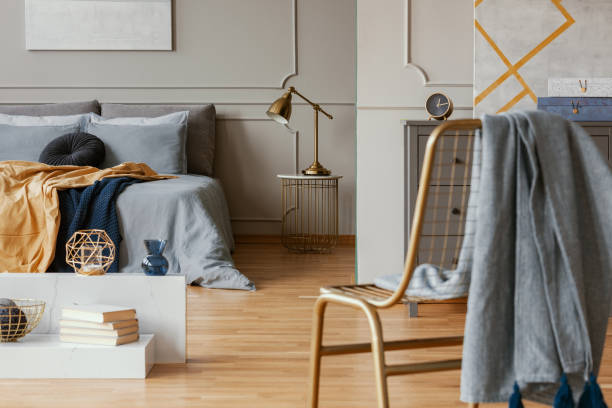 istock Blanket on golden chair in bright bedroom interior with grey wall 1161170072