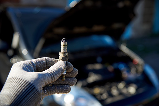 Spark plug for engine in male hand on the background of a car with an open hood.