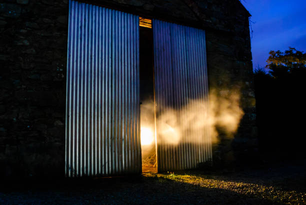 Light shines out from half open doors of an old Irish stone barn at night