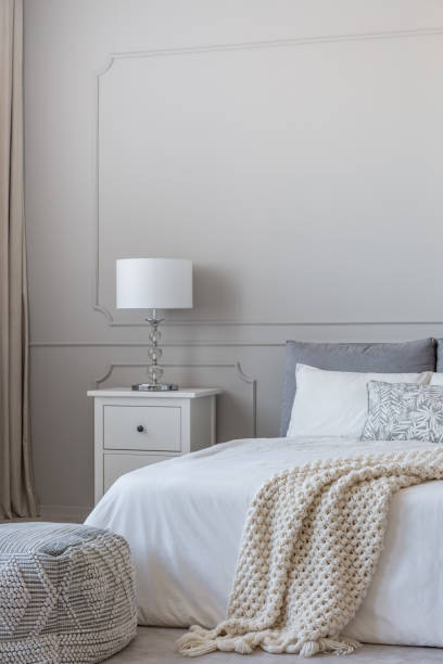 istock Simple white lamp on wooden night stand table with two drawers next to comfortable king size bed with cozy bedding 1161171383