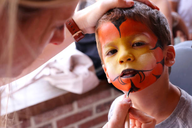 Little boy having his face painted Artist painting a little boys face as a tiger or a lion cat face paint stock pictures, royalty-free photos & images