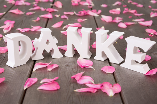 Thank you word in german, letters in 3d standing on real rose petals and wodden board