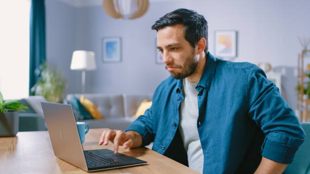 istock Portrait of Handsome Young Man Using Laptop Computer at Home, Making a Sad Face and Regret about His Loss. Cozy Modern Flat done in Scandinavian Style. 1161176784