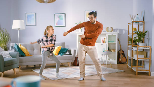 happy little girl dances with young father in the middle of the living room. happy family time, father and daughter dancing at home. - pai e filha a dançar imagens e fotografias de stock